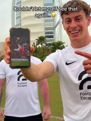 A man holding a smartphone displaying a red and white football, with skyscrapers and trees in the background