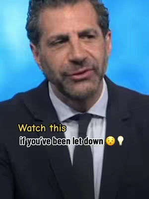 A medium shot featuring a man in a dark suit addressing the camera. Above the main subject, overlaid text appears to convey the video's message. The background is a solid blue.