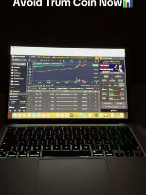 A laptop displaying a trading interface is open on a dark surface. The screen shows financial data with charts and numbers. Text overlay indicates a warning about a 'Trum Coin' and indicates the location.