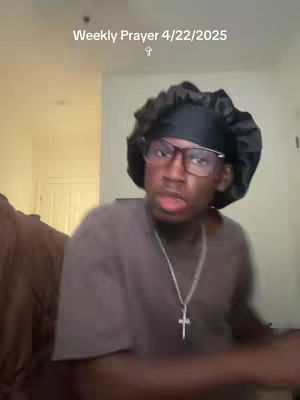 A man wearing glasses, a black durag, and a silver cross necklace is looking at the camera. Above him, the text "Weekly Prayer 4/22/2025" with a small cross symbol.