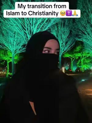 A woman wearing a black hijab and a black garment stands in front of a blurred background of vibrant green trees. The text overlay at the top reads, "My transition from Islam to Christianity."