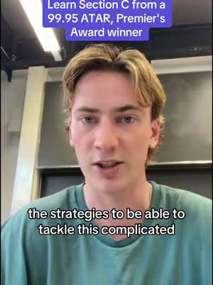 A young man with light skin and short, unkempt blond hair is centered in the frame. He wears a simple, teal-colored t-shirt. Above him, a text overlay in a blue box reads: 'Learn Section C from a 99.95 ATAR, Premier's Award winner.' Below him, another text overlay states: 'the strategies to be able to tackle this complicated.' The background is a blurred office or classroom setting. The lighting appears to be bright and natural.
