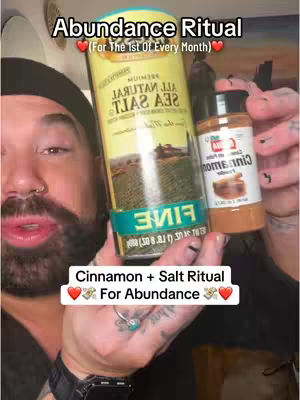 A selfie-style shot featuring a man holding up a large container of salt and a small bottle of cinnamon. Text overlays state the ritual being performed and the desired outcome of prosperity. The man has a neutral expression with a slight smile, and there are tattoos visible on his right hand.