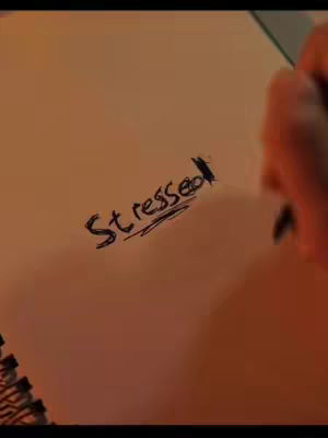 The cover image showcases a hand writing the word "Stressed" on a white notepad. The hand is holding a pen, and the image has a warm, yellowish tint.