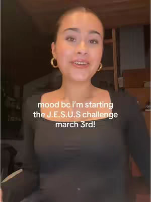 A young woman with light skin and dark hair is centered in the frame. She wears gold hoop earrings and a black long-sleeved top. Text overlaid on the image reads, 'mood bc i'm starting the J.E.S.U.S challenge march 3rd!' The background is dimly lit, with hints of a room visible.