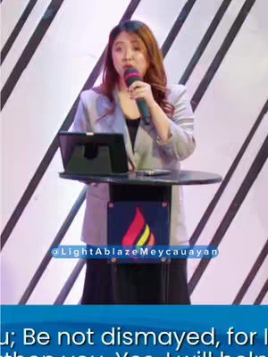 The image features a woman speaking into a microphone from behind a lectern. The background has a diagonal striped pattern. A blue banner with white text at the bottom of a screen, and a logo.