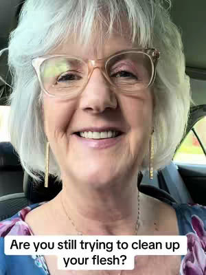 A mature woman with short, white hair wearing glasses smiles directly at the camera. The background shows a car interior. Text across the bottom asks a question about cleaning up flesh, overlaid on the video.