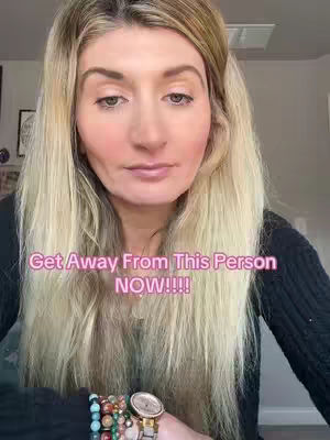 A woman with long blonde hair looks directly at the camera. Text overlayed on image: Get Away From This Person NOW!!!! She's wearing a black top and a watch and bracelets are visible on her wrist.