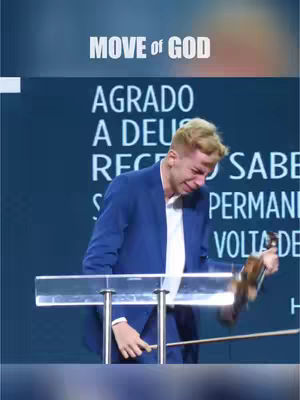 The image captures a man on stage, overcome with emotion. He appears to be weeping, his face contorted with tears. He is holding a violin and bow, seemingly in the middle of a performance. The background features an expansive wall with large text in a foreign language.