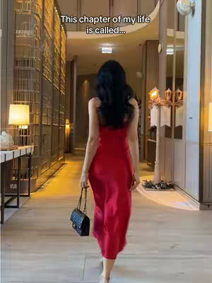 A woman in a red dress walks away from the camera in a well-lit hallway. The hallway has architectural details and a luxurious aesthetic.