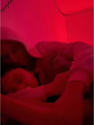 A blurry, intimate shot of a couple. The image is completely saturated with red lighting, which obscures details but suggests a warm, romantic, and private setting. The bodies of two people are intertwined, suggesting cuddling or closeness. The scene is dimly lit, and the overall composition emphasizes intimacy and emotion.
