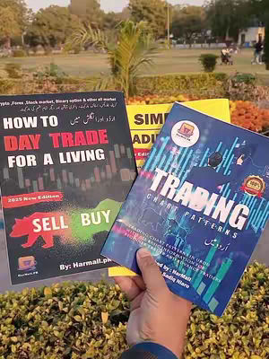 A person holding two books with trading-related titles. The background shows a park with trees and bushes, suggesting an outdoor setting. The person's hand is visible, holding the books up for display. The books' covers are colorful, with text emphasizing key concepts in day trading and trading patterns.
