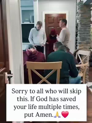 A group of people in casually dressed are gathered in a living room, the focus is on a wooden dining chair, and the group seems to be engaged in a prayer or religious service.