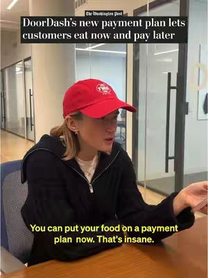 A woman in a red baseball cap and black jacket sits at a desk, looking off to the side with a serious expression. Text overlays indicate information about a partnership with DoorDash for a payment plan, and the logo for the Washington Post is visible. A plain office setting provides the backdrop. The color scheme is muted with neutral tones, with the red cap being a focal point.