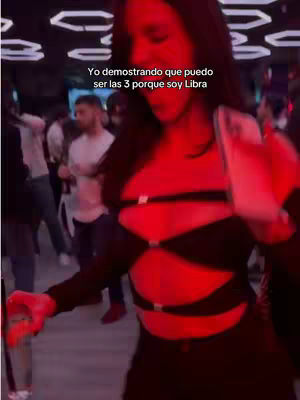A woman in a black top and skirt is dancing in a nightclub setting. The scene is lit with red lights. Text overlay is present at the top.