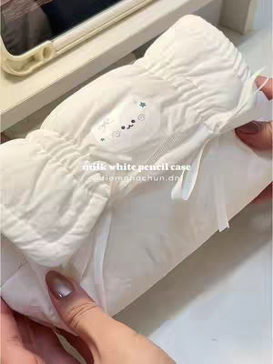 The cover image shows a close-up of a soft, white pencil case. The case is textured with a quilted design, and has a small, round patch with a cartoon face embroidered on it. A hand holds the pencil case open, revealing the inside, and shows a tablet in the background.