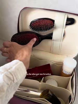 A close-up shot inside a makeup case, revealing brushes and other beauty products. The case is open, with a hand reaching in to touch a brush. The background is a soft, neutral color.