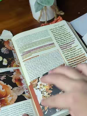 The image features an open Bible with colorful floral scrapbook paper used as tip-ins or bookmarks. The pages are filled with handwritten notes and highlighted text, indicating someone is studying or journaling. A hand is visible, likely of the video creator, interacting with the Bible pages.