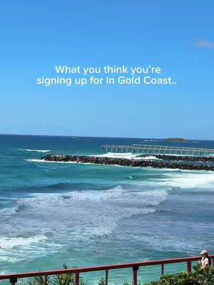 A scenic shot of a beach with a clear blue sky. The ocean waves are crashing onto the shore, and there's a pier in the distance. The image has a bright and sunny feel.