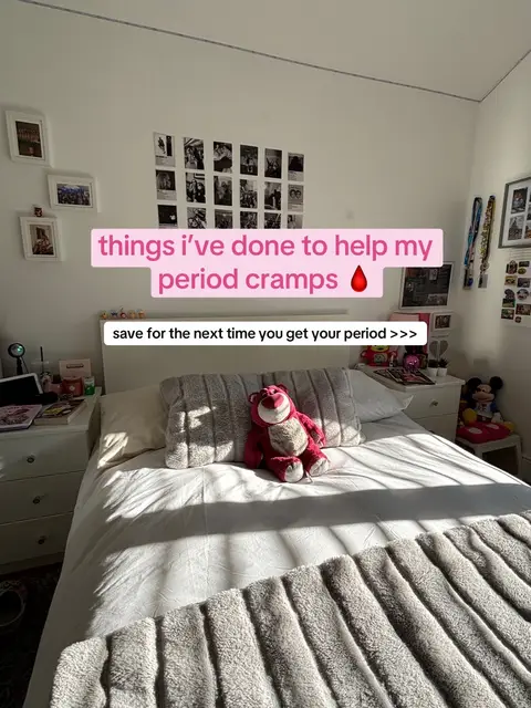 The cover image shows a bedroom interior, primarily featuring a bed with white bedding and a gray fuzzy blanket at the foot. A large, plush pink toy is placed on the bed. Text overlays on the image, highlighting solutions for period cramps.