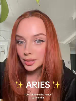 A woman with long red hair looks directly at the camera. The image is framed from the chest up against a light background. Text overlay in white and yellow stars reads "ARIES" and "I don't know who needs to hear this".
