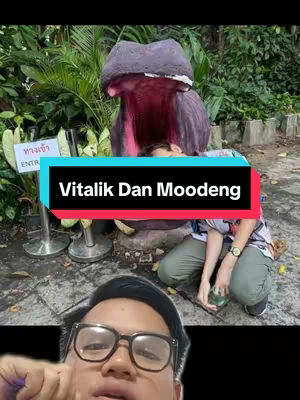 The cover image features a man's face in the foreground. A black and blue banner overlays the image with the text 'Vitalik Dan Moodeng'. In the background, there's a hippo statue with an open mouth and a person crouching beneath the hippo. The background suggests a park setting.