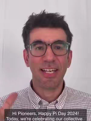 A man with glasses and a patterned shirt speaks to the camera against a white background. A text box at the bottom of the screen displays text.