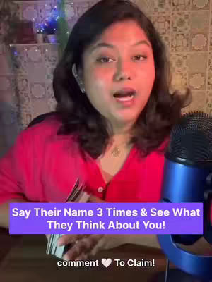 A woman with dark hair and fair skin is centered in the frame, looking directly at the camera with an open mouth, as if speaking. She is wearing a pink button-down shirt and has a necklace in place. To the right of her, a blue microphone stands tall. In the forefront, a portion of a tarot deck is held in her hands. At the lower third of the image runs a text overlay in purple indicating the video's content.