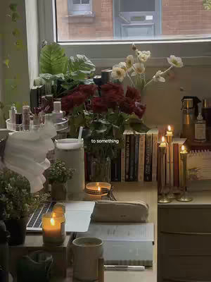 A cozy study desk, bathed in soft light, features a laptop, books, candles, and fresh flowers, creating a serene and inspirational study environment.