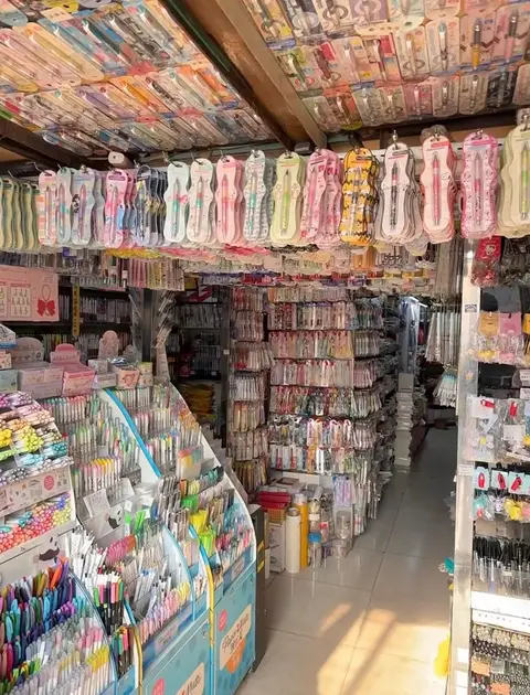 A shop interior filled with stationery supplies. The ceiling is covered with items, and rows of pens are displayed on shelves and in display cases.