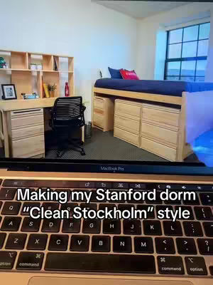The cover image shows a laptop keyboard at the bottom, with a dorm room interior visible above it. The room features a desk, bed, and shelves, all made of light-colored wood, suggesting a minimalist design. The bed has blue bedding and a red accent pillow. The room is well-lit, with a window offering a glimpse of the outside.