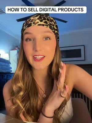 A young woman with long blonde hair and a patterned headscarf smiles directly at the camera. She is wearing a light-colored top and several rings. In the background, a ceiling fan is visible.