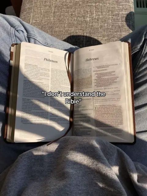 The image shows an open Bible on a person's lap, with the text "I don't understand the Bible" overlaid. The Bible is open to the books of Philemon and Hebrews, with a bookmark in place. The lighting suggests a sunny environment.