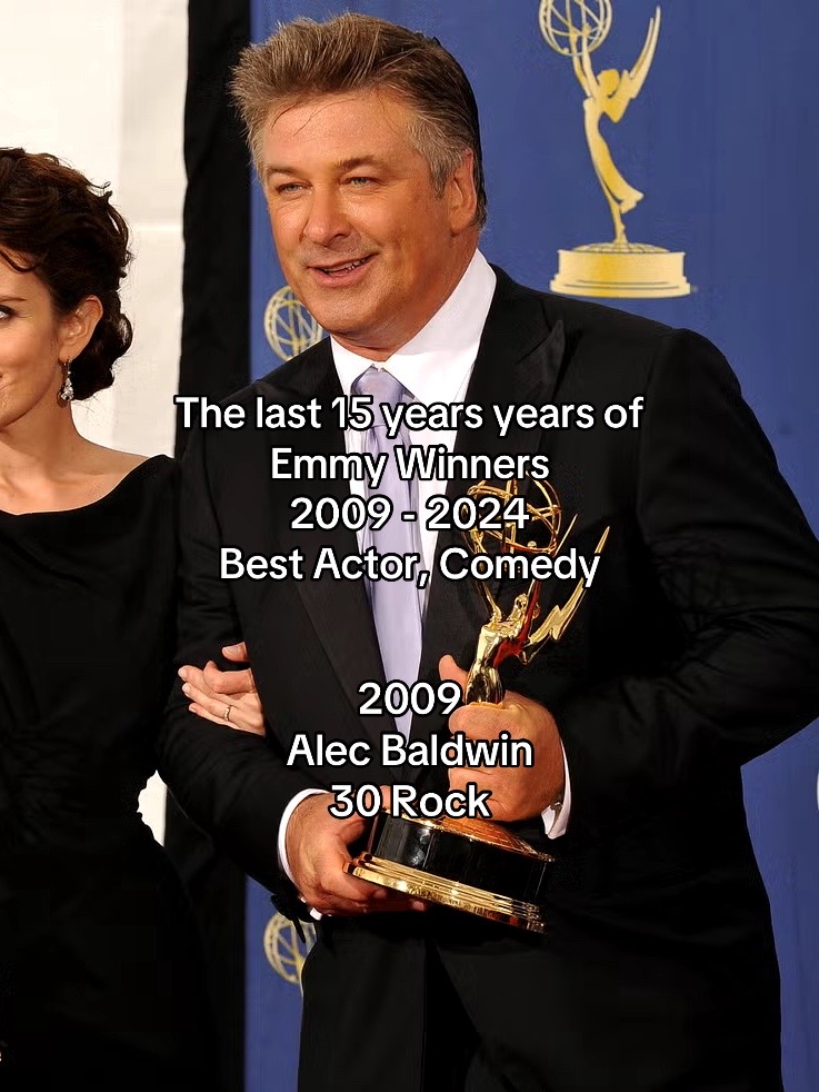 The image shows Alec Baldwin in a suit, holding an Emmy award while smiling slightly. Text is overlaid, listing Emmy winners and category information.