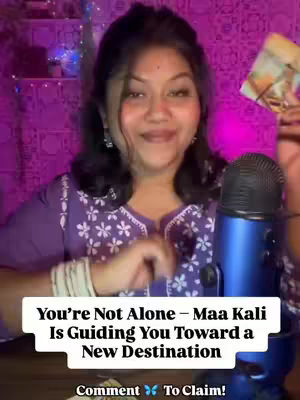 A woman with dark hair and a traditional Indian outfit stands in front of a purple background, holding a card and a microphone. Text overlays indicate she is a psychic reader and that the video is about the guidance of Maa Kali.