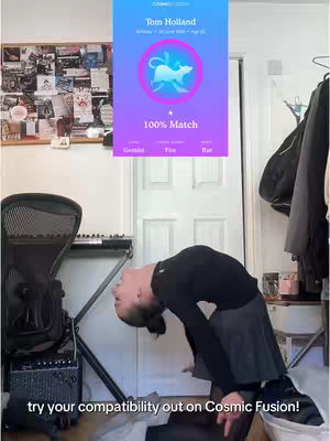 A person, with their head bent backward in an arch, is the primary focus. They are wearing a black top and a grey skirt. Behind them is a room with a busy wall with posters and an app screen displaying a compatibility check for a celebrity.