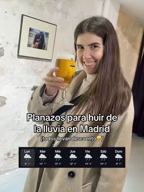 A woman with long brown hair is holding a glass of beer, smiling at the camera. The background is a light-colored wall with a framed picture. Text overlays the image, and there is a weather report graphic at the bottom.