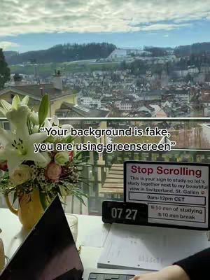 The cover image shows a well-lit room with a bright outdoor scene visible through a window. A bouquet of white lilies and other flowers is arranged in a yellow vase. On a white surface is a laptop, a desk clock displaying 07:27, and a small sign that says "Stop Scrolling". The background outside the window shows a town nestled in a valley amidst rolling green hills, suggesting a scenic location suitable for studying.