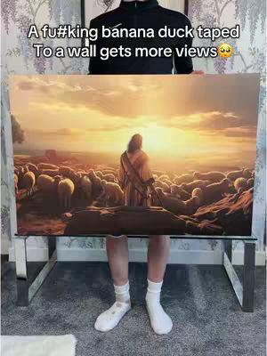 A man stands in front of a large painting depicting Jesus with a flock of sheep. The man is wearing a black jacket, white socks, and white shoes. The image is in a room with patterned wallpaper and a glass table.