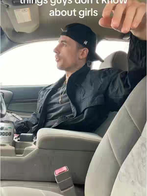 A man in a black baseball cap and jacket sits inside a car, looking to his left. The car's interior is visible, with a light-colored seat and center console. Text overlayed on the image reads, 'things guys don't know about girls'.