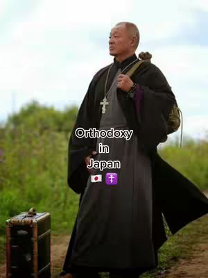 A man in religious attire stands outdoors. He wears a dark robe, holds a cross necklace, and carries a backpack. Text overlays read 'Orthodoxy in Japan' with Japanese and Orthodox cross symbols.