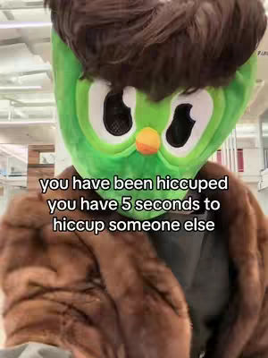 A person wearing a large, green, owl-like mask with big eyes and a small orange beak. The person is wearing a brown fur coat. Text overlayed on the image reads, "you have been hiccuped you have 5 seconds to hiccup someone else."