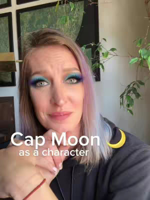 A woman with light skin and blonde hair with shades of lavender. She wears bold, colorful eye makeup. She appears to be in a well-lit indoor space, likely a home. Text overlays appear in the image.