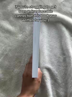 The cover image shows a hand holding a book, with the edge facing the camera. The background is a textured, light-colored fabric, possibly a blanket or sheet. The book is white, and the text is a black overlay.