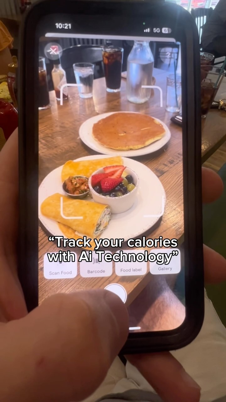 A person holds a smartphone displaying an app interface at a restaurant table with breakfast food on a plate. The app seems designed to track calories by scanning food. Text overlayed on the image prompts the user to track calories using AI technology.