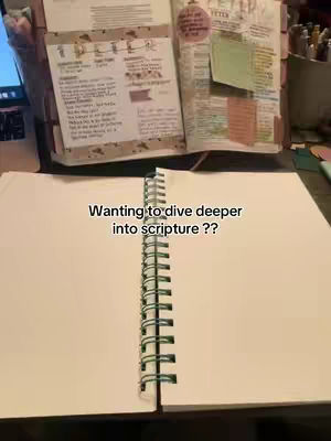 The image shows an open notebook with blank pages in the foreground. A spiral binding runs down the spine. In the background, another book is open, with colorful sticky notes and annotations visible on its pages. Text overlaid on the notebook says, "Wanting to dive deeper into scripture ??".