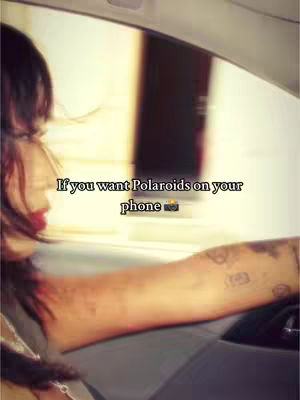 A woman is driving a car, with tattoos on her left arm. The image has a warm, retro filter applied. Text overlayed on the image reads: "If you want Polaroids on your
phone 📸".