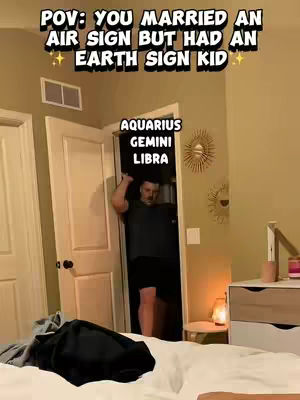 The image shows a man standing in a doorway with text overlays. He is in a dimly lit room, likely a bedroom, with a bed, a bedside table with a lamp, and a decorative sunburst on the wall. The text at the top reads, 'POV: YOU MARRIED AN AIR SIGN BUT HAD AN EARTH SIGN KID'. Below this, in a separate box, are the words 'AQUARIUS, GEMINI, LIBRA'.