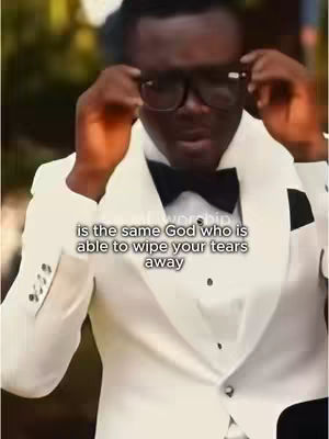 A man in a white tuxedo adjusts his glasses. Overlaid text states: "is the same God who is able to wipe your tears away."