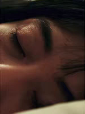 The image shows a very close-up view of a person's face, with the focus on the eye, nose, and mouth area. The skin tone appears to be warm, and slightly blurred, suggesting a soft focus. The person's eyes are closed, conveying a sense of rest. The lighting appears to be soft. The composition is simple, the angle is from close to the eye level.